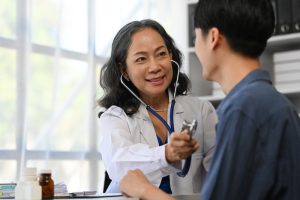Positive mature doctor using stethoscope, listening to male patient breath or heartbeat. Healthy care concept